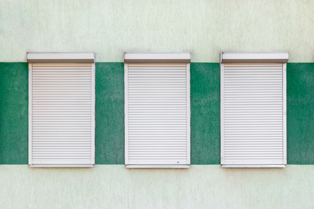Drei geschlossene weiße Rollläden an einem grün gestrichenen Haus.