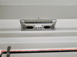 Detaillierte Ansicht einer Türschließe aus Metall, montiert an einer Holztür, zeigt Mechanismus und Sicherheitsmerkmale.