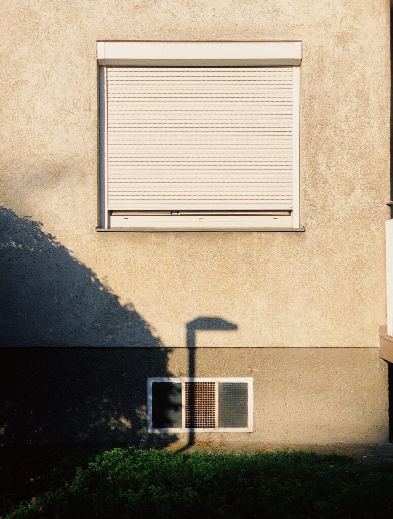 Geschlossener Rollladen an einem Fenster einer Hausfassade mit Schatten.